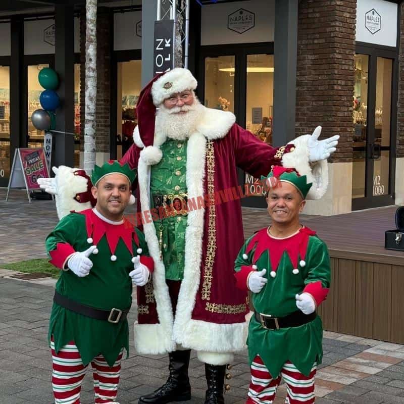 Santa standing outdoors between two elves giving thumbs up.