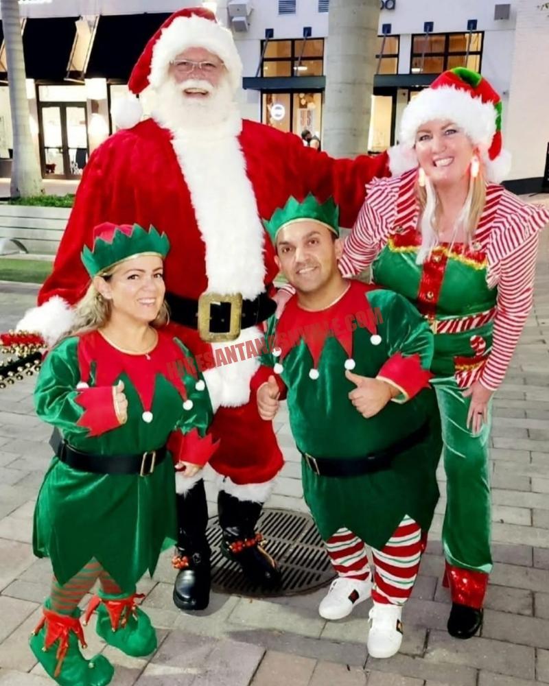 Santa for hire in Murfreesboro, TN: Santa outdoors with three elves at dusk by a storefront.