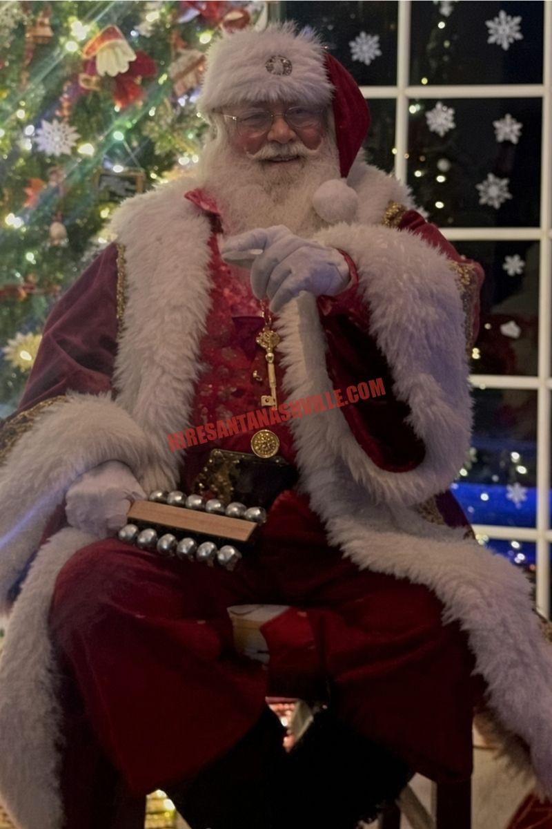 Santa for hire in Brentwood, TN: Santa seated with sleigh bells by a tree and a night window.